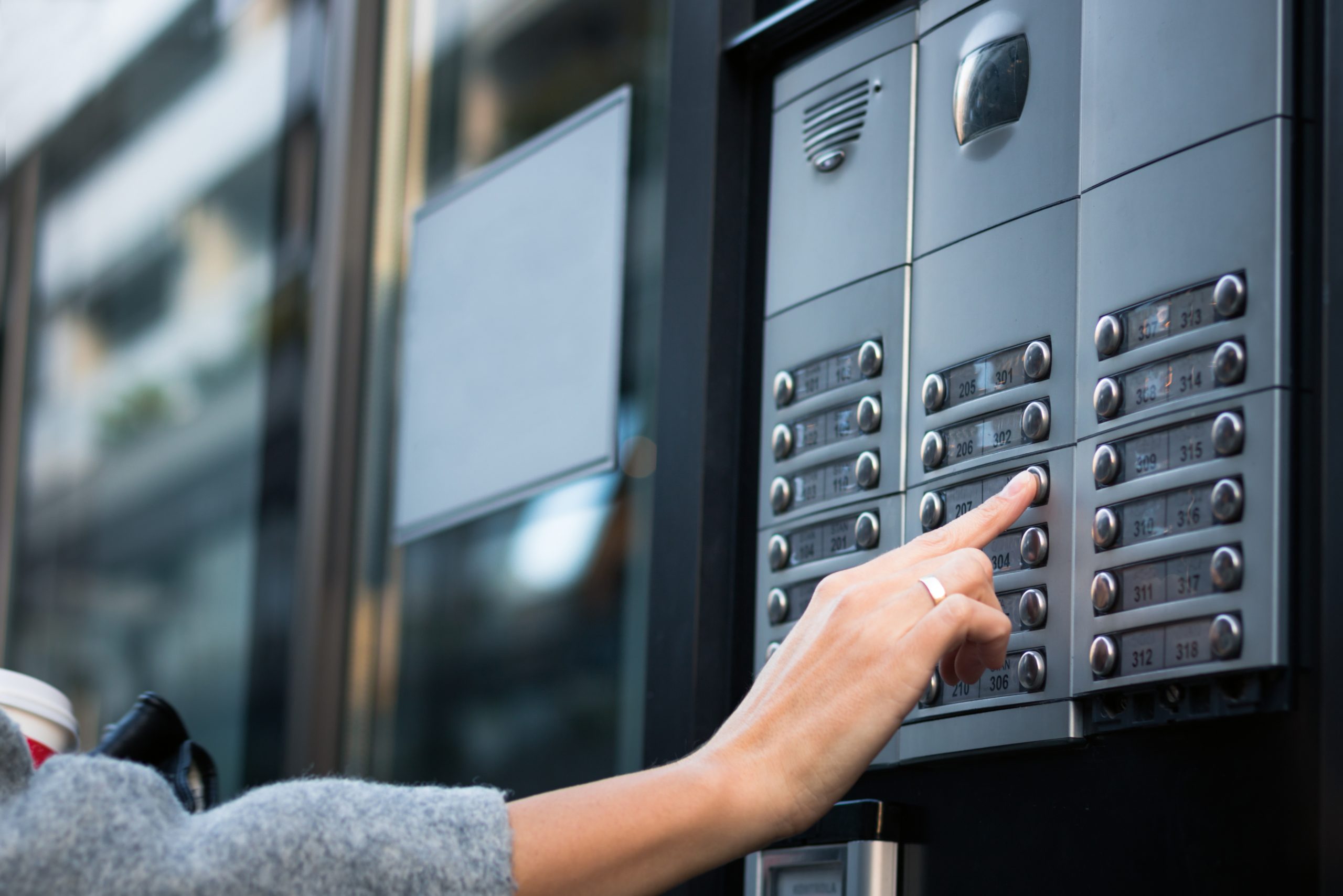 Close up of woman using intercom at residential building entrance.